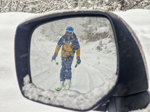 Skier reflected in car mirror during snowy mountain drive
