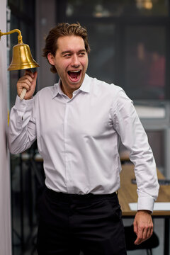 Young man ringing brass service bell with excited expression inside office or restaurant interior, with man, adult, male, shirt detail, showing dress, trouser, black, white context