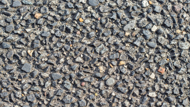 Close up shot of dark grey asphalt road surface showing rough gravel texture with stone texture pavement pebblestones transportation infrastructure driveway material