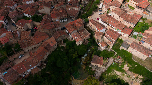 aerial view of a historic village with red-tiled roofs and stone buildings in a peaceful and serene setting, captured from above, Risco los camellos, Cascada de Orbaneja del Castillo