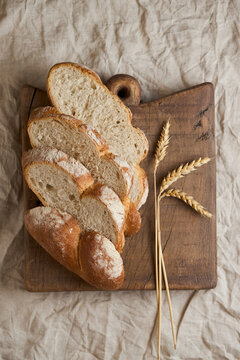 Rustic sliced bread loaf on wooden board with wheat