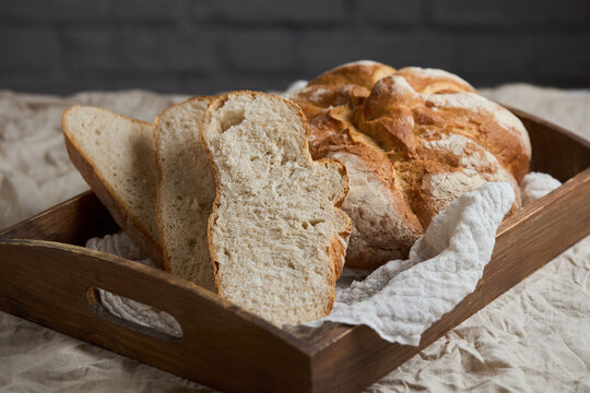 Rustic artisan bread loaf and slice in wooden tray