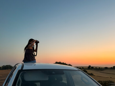 Woman photograph sunset from car roof in countryside
