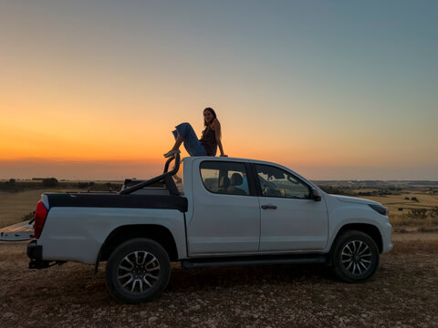 Woman on pickup truck roof at sunset countryside