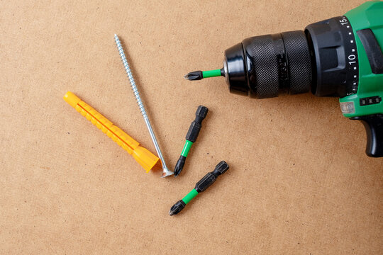 Green cordless drill with bits, screw, and orange dowel
