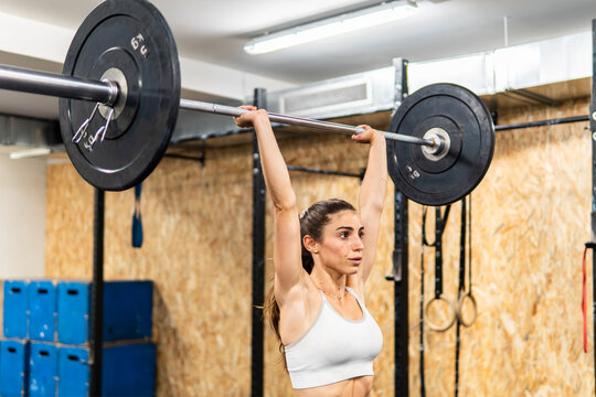 Woman perform overhead barbell lift in fitness gym