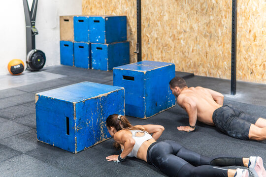 Couple perform push-ups beside plyometric boxes in gym