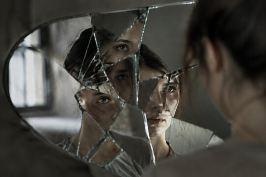 Shattered mirror reflecting fragmented facial features with soft window lighting.