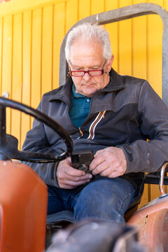 Senior farmer use smartphone on tractor in countryside