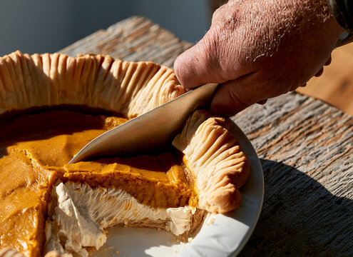 close up of a hand cutting a freshly baked pumpkin pie with a kitchen knife
