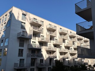 A white multi-story apartment building with balconies and glass doors against a clear blue sky...