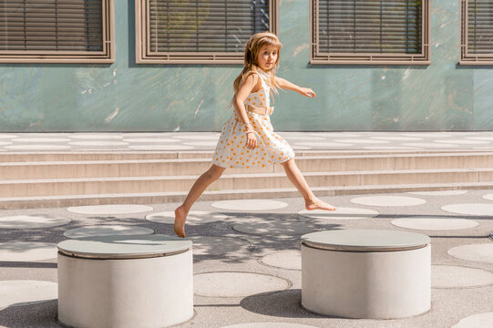 Girl leap between platform in summer city courtyard