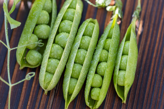 Fresh green pea pods with water droplets on wood