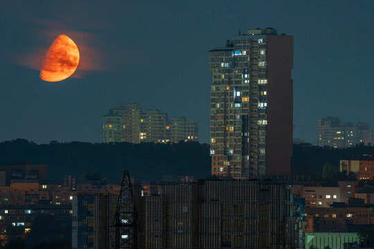 Dramatic large orange moon rising over modern city skyscrapers at night
