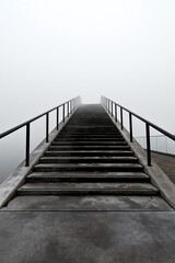 Fototapeta premium Concrete staircase ascending upward into dense white foggy atmosphere