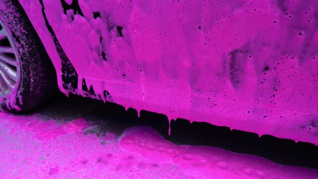 Car wash with pink foam cleaning a vehicle