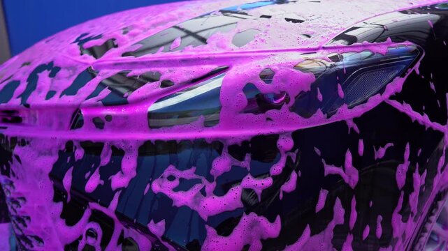 Car wash with pink foam on a black vehicle headlight