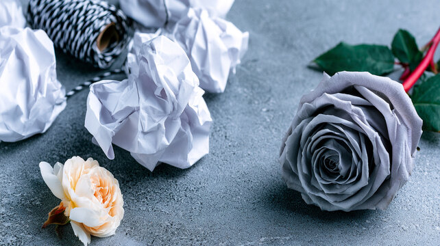 Artificial grey rose flower crafted from paper next to crumpled paper balls on concrete surface