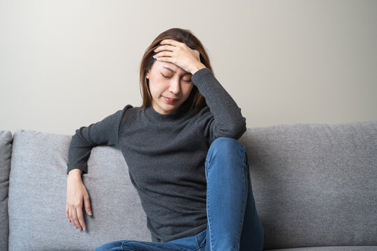 Unhappy anxiety young Asian woman covering her face with pillow on the cough in the living room at home.