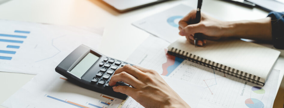 Women business people use calculators to calculate the company budget and income reports on the desk in the office.