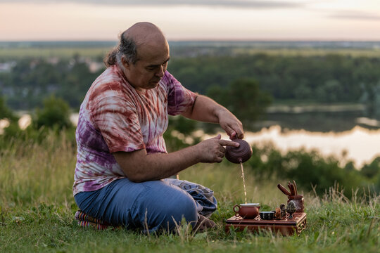 Man performs tea ritual outdoors overlooking tranquil lake