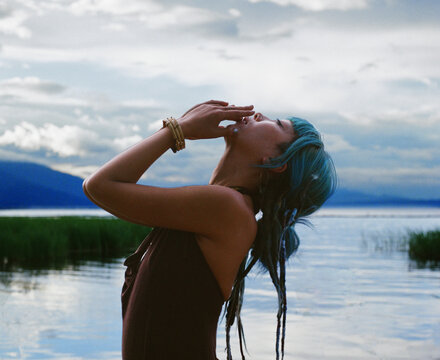 Blue Haired Woman in Contemplative Pose by Quiet Lakeshore