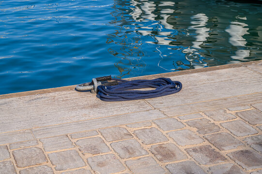 Blue mooring rope coiled on a dock next to calm blue water
