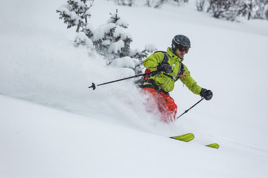 Freeride skier carving deep powder in alpine forest