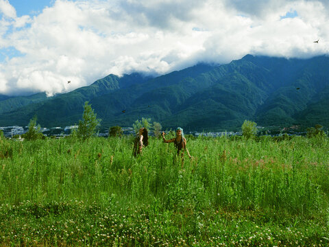 Two Friends Standing in Meadow Beneath Dramatic Mountain Clouds