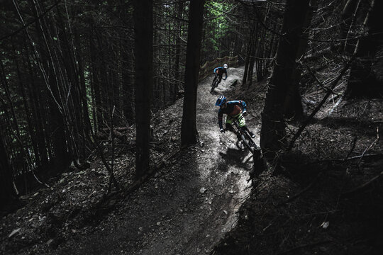 Two mountain bikers riding enduro bikes through a bike park trail,