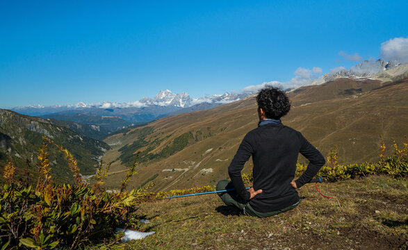 Rear view of a hiker sitting on hill enjoying Mount Ushba landscape view in Svaneti Georgia.