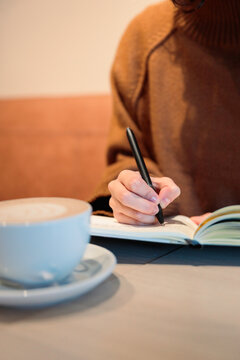 Woman holding pen over notebook at cafe