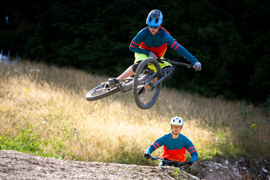 Two mountain bikers jumps a big transfer. One make a Table top trick.