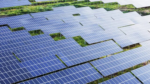 Aerial forward movement over an extensive photovoltaic solar panel array in a lush green field, highlighting renewable green energy and sustainable power generation infrastructure.