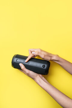 Woman hands operating portable Bluetooth speaker on yellow background