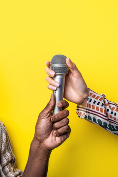 Multiethnic hands holding microphone against yellow background