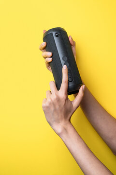 Woman hands adjust portable Bluetooth speaker on yellow background