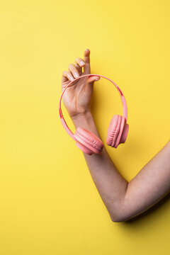 Woman hand holding pink headphones on yellow background
