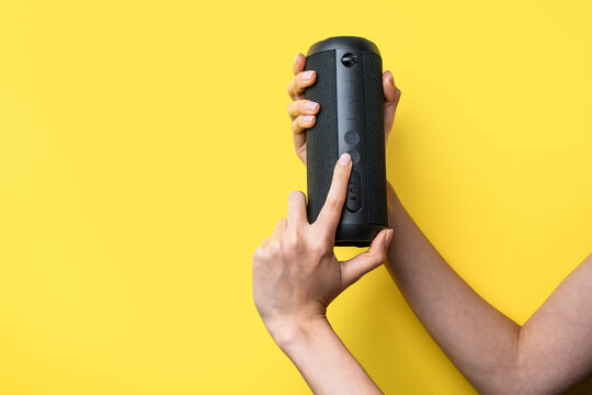 Woman hands adjust portable Bluetooth speaker on yellow background