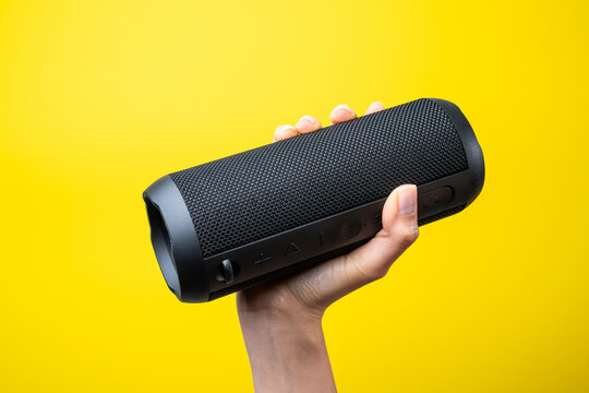 Woman hand holding portable wireless speaker on yellow background