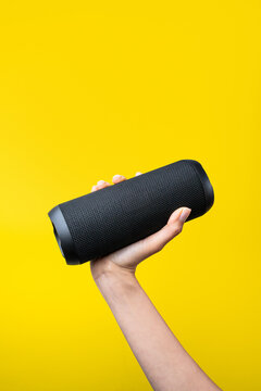 Woman hand hold portable wireless speaker on yellow background