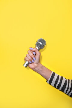 Woman hand hold microphone on yellow background