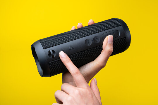 Woman hands adjust portable Bluetooth speaker on yellow background