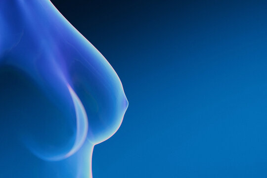Abstract close-up of a female breast form glowing with cool blue neon light against a dark blue gradient. Creative image represents breast health screening and medical imaging concepts.