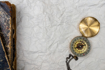 Vintage compass and pocket watch on crumpled paper beside an antique book. Exploration, history, time, navigation, nostalgia, travel, adventure, and discovery concept with copy space. © Svetliy