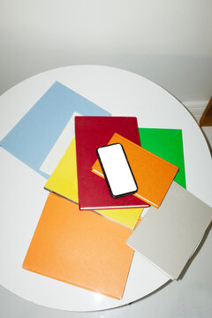 Smartphone mockup in table with colourful books and magazines