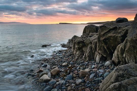 Sunset at Salthill Beach along the Wild Atlantic Way, Galway Ireland with glowing orange sky, calm shoreline, rugged rocks and peaceful coastal atmosphere, travel Europe
