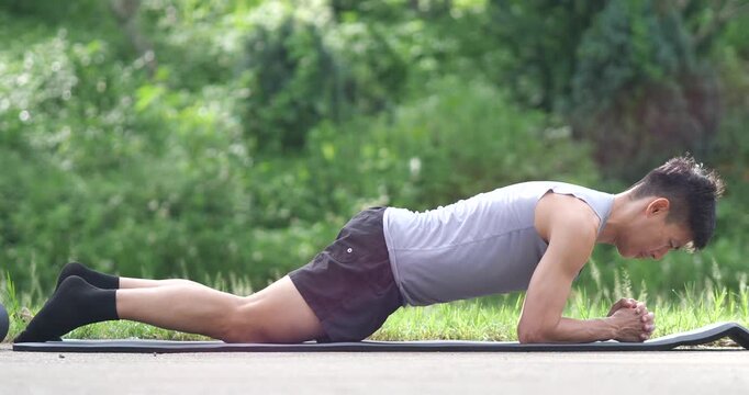 Side view of athletic man doing knee forearm plank exercise on mat in park