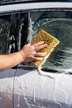Hand wash car window with sponge and soap outdoors