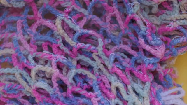 Close-up of a wet multi-colored knitted fishnet of blue, pink and white threads in water